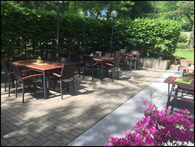 Terrasse vor dem Volkshaus mit Tischen im Schatten der Bäume.